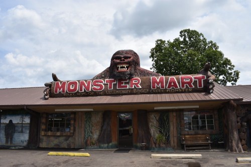 A quirky store called "Monster Mart," featuring a large, playful Bigfoot statue on the roof and a rustic facade.
