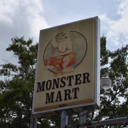 Sign for "Monster Mart" featuring a cartoon yeti riding a pig, set against a cloudy sky.