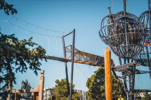 A playground structure featuring a rope bridge and a large spherical climbing frame against a clear blue sky.