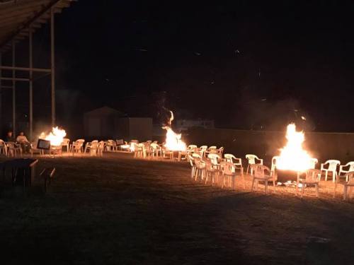 A nighttime scene with several chairs arranged around large bonfires, creating a warm, inviting atmosphere.