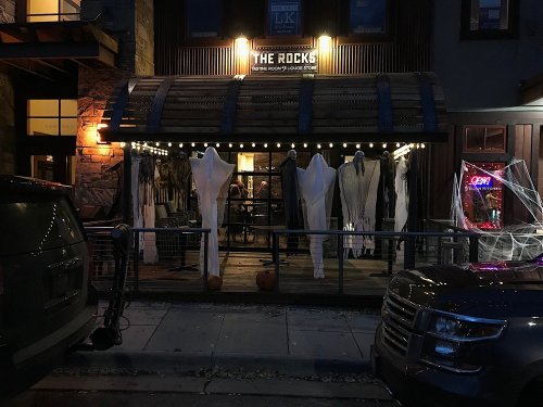 A dimly lit restaurant entrance decorated with ghostly figures and Halloween decor, with a neon "OPEN" sign.