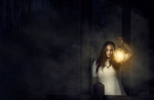 A woman in a white dress holds a lantern, standing in a dark, misty environment.