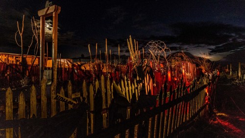 A spooky night scene featuring a dimly lit fence surrounded by eerie decorations and a full moon in the background.