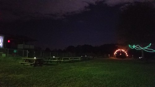 A dimly lit outdoor area with picnic tables, a glowing arch, and colorful lights against a night sky.