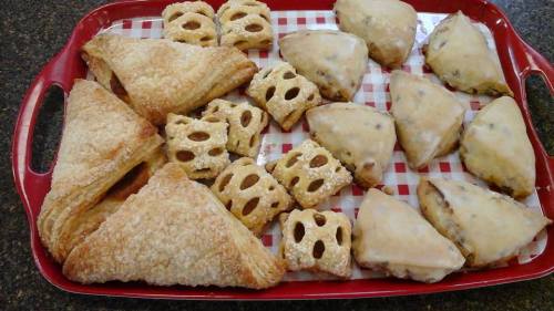 A red tray filled with assorted pastries, including flaky triangles and glazed treats, arranged on a checkered paper.