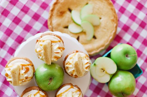 A display of apple pie, green apples, and caramel apple cupcakes on a checkered tablecloth.