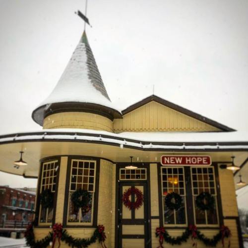 A charming, snow-covered building with a pointed roof, decorated for Christmas in New Hope. Wreaths adorn the windows.