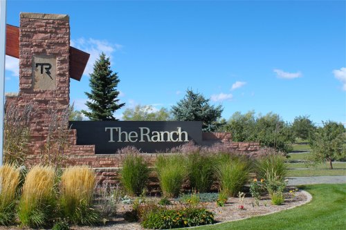 Sign for "The Ranch" surrounded by greenery and blue sky, featuring decorative landscaping and trees.