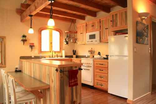 Cozy kitchen with wooden beams, light cabinets, and a white fridge, featuring a small dining area with bar stools.