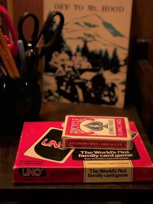 A table with a stack of games: UNO and a deck of playing cards, with scissors and pens in the background.