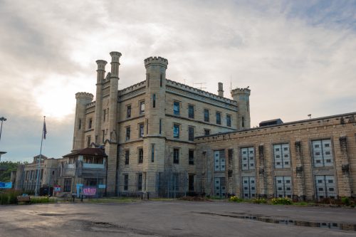 Historic stone building with towers, surrounded by a fence, under a cloudy sky.