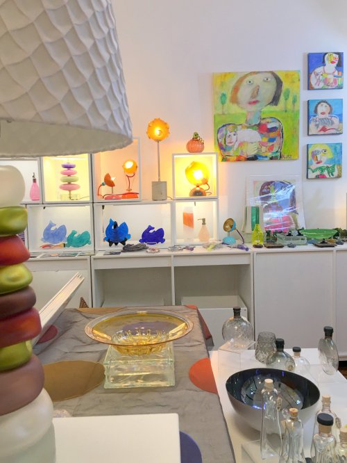 A colorful art studio featuring glass objects, paintings, and decorative lamps on display.