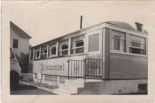 A vintage diner on a street, featuring large windows and a sign that reads "Pleasant." Black and white photo.