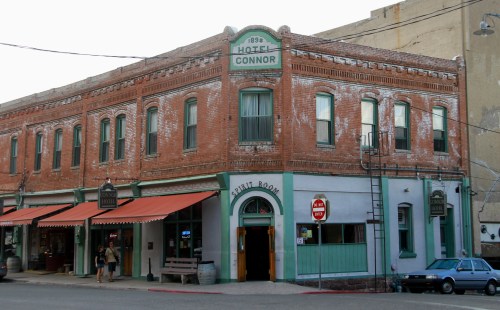 Historic brick building with green accents, featuring "Hotel Connor" sign and awnings, located on a street corner.