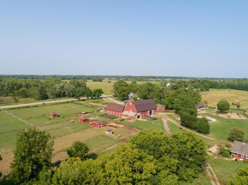 Aerial view of a red barn surrounded by green fields, trees, and small animal enclosures on a sunny day.