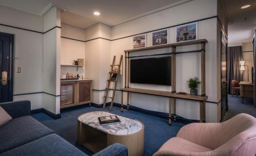 A cozy hotel room featuring a seating area, a TV on a wooden stand, and a small kitchenette with modern decor.