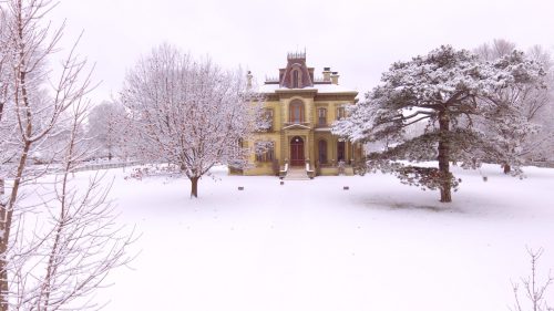 A grand, historic house surrounded by snow-covered trees and a white landscape on a winter day.