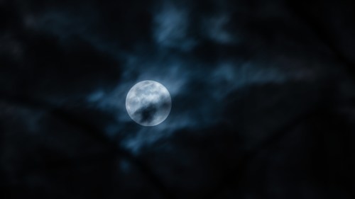 A bright full moon surrounded by dark, swirling clouds in a night sky.