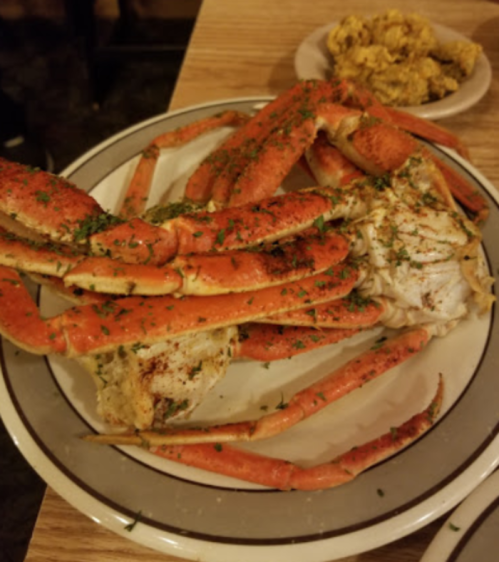 A plate of steamed crab legs garnished with herbs, accompanied by a small dish of dipping sauce.