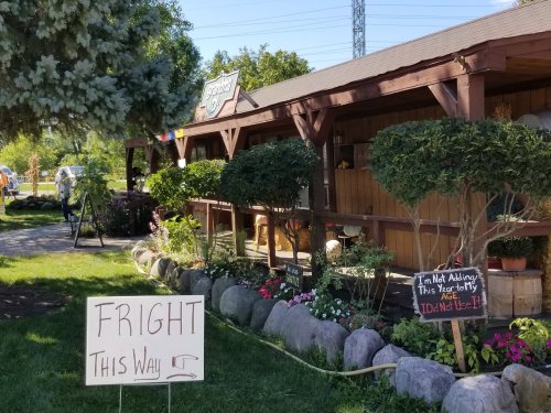 A rustic building with a sign reading "Fright This Way" and a humorous note about not adding to the scare.