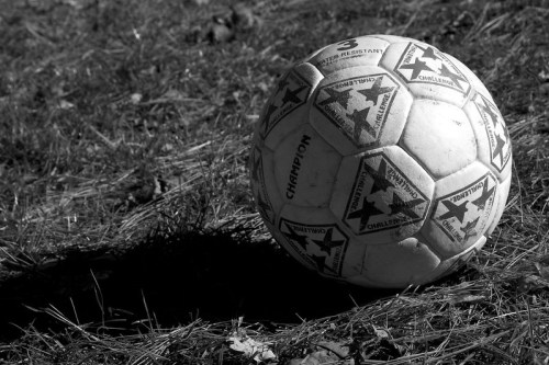 A worn soccer ball resting on grass, captured in black and white.