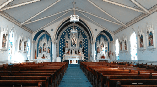 Interior of a church featuring ornate decorations, a central altar, and rows of wooden pews.