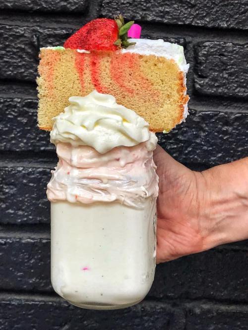 A hand holding a mason jar filled with whipped cream and a slice of cake topped with a strawberry.