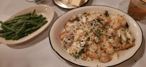 A plate of shrimp and crab topped with creamy sauce, served with green beans on the side.