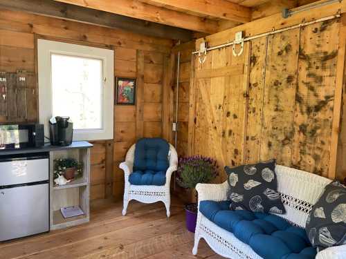 Cozy interior of a wooden cabin featuring a small kitchenette, two white wicker chairs, and a window with natural light.