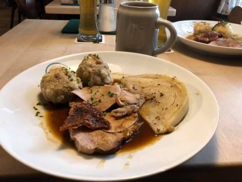 A plate of sliced meat with crispy skin, dumplings, and cooked cabbage, served with a rich brown sauce.