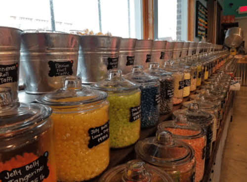 A colorful display of jars filled with various candies and taffy, lined on a wooden shelf in a shop.