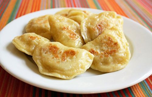A plate of golden-brown dumplings, lightly pan-fried, on a colorful striped tablecloth.