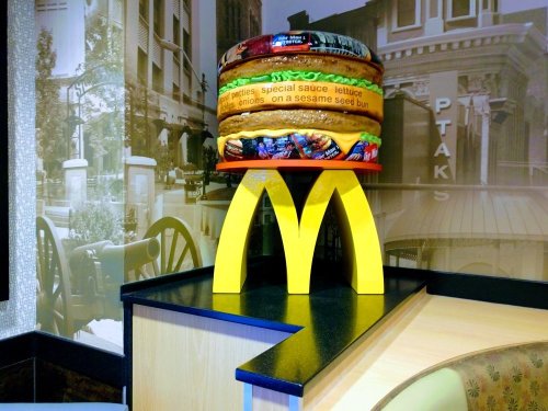 A colorful McDonald's display featuring a large burger model on a yellow arch base in a restaurant setting.