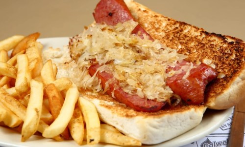 A toasted sandwich with sausage and sauerkraut, served with a side of golden French fries.