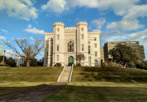 A grand castle-like building with turrets, set against a blue sky and grassy landscape.