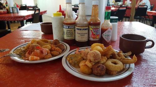 Two plates of seafood with various sauces and condiments on a red table, alongside a cup of coffee.