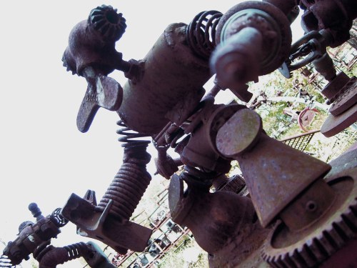 A whimsical robot sculpture made from various metal parts and springs, set against a blurred outdoor background.