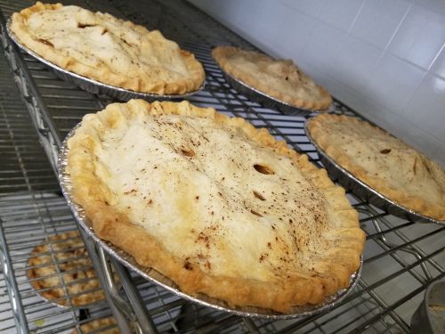 Four freshly baked pies cooling on a wire rack, with golden-brown crusts and a few small vents on top.