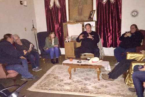 A group of people sitting in a dimly lit room, engaged in conversation around a coffee table.