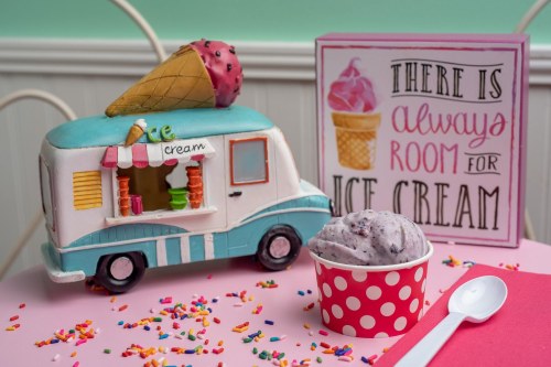 A colorful ice cream truck cake with a cone on top, surrounded by sprinkles and a sign that says "There is always room for ice cream."