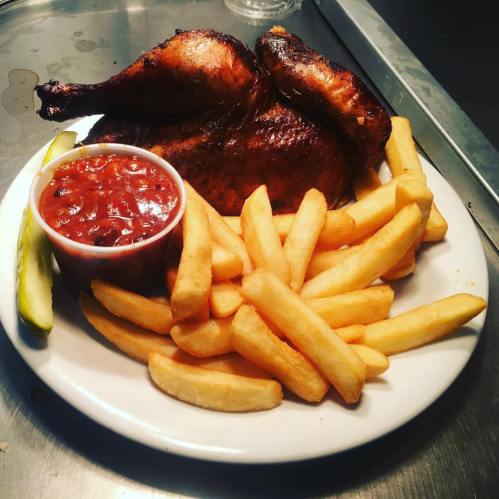 A plate of roasted chicken with fries, a side of pickles, and a small bowl of barbecue sauce.