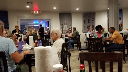 A busy restaurant scene with diverse patrons dining at tables, some enjoying meals and others engaged in conversation.