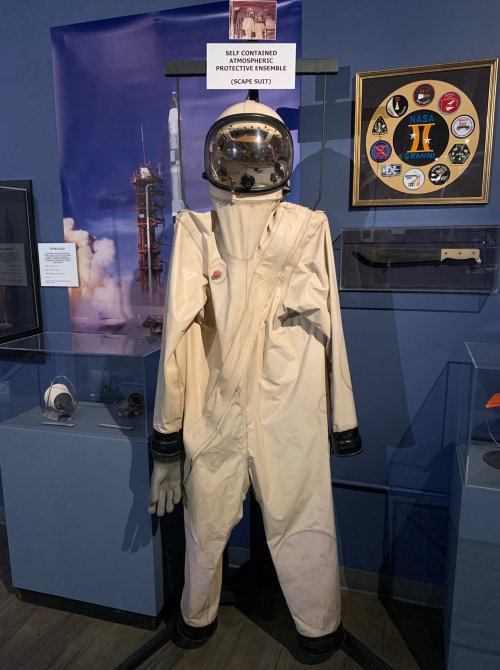 A display of a beige space suit on a mannequin, labeled "Suit Contained Protective Ensemble (SCAEP Suit)."