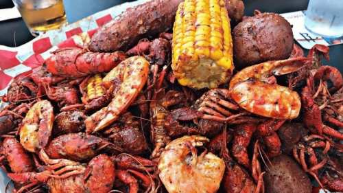 A vibrant seafood platter featuring crawfish, shrimp, corn, and sausage, served on a red and white checkered paper.