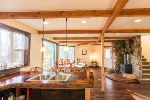 Cozy kitchen with wooden beams, a stone fireplace, and a dining area featuring large windows and natural light.