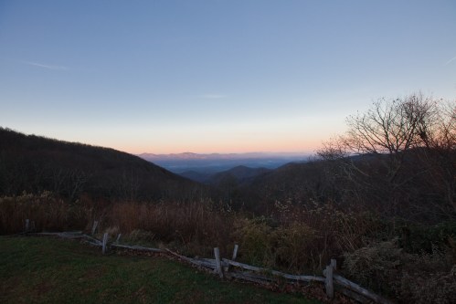 A serene mountain landscape at dusk, with rolling hills and a colorful sky fading into twilight.