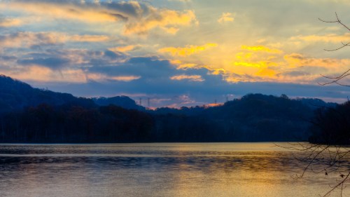 A serene lake at sunset, with colorful clouds reflecting on the water and hills in the background.