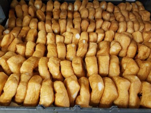 A close-up view of a large tray filled with golden-brown, fluffy bread rolls arranged neatly in rows.
