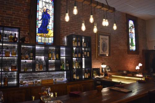 A cozy bar with a wooden counter, illuminated shelves of liquor, and stained glass windows. Warm lighting creates an inviting atmosphere.