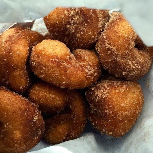 A close-up of golden-brown, sugar-coated doughnut holes in a paper bag.